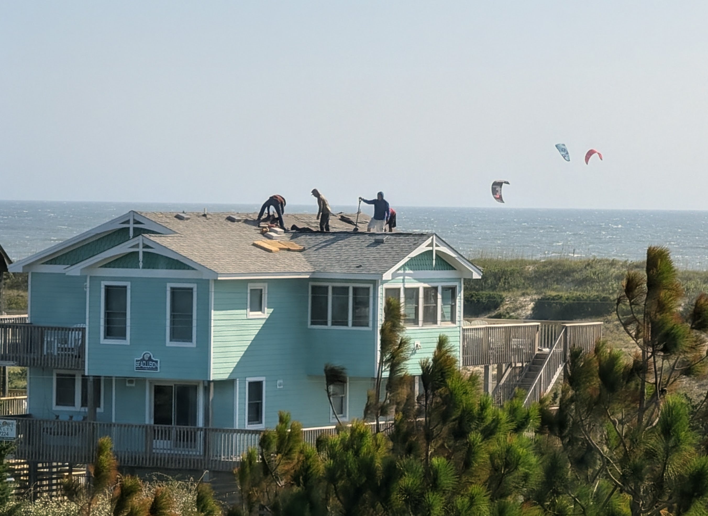 Roofers working on house with kiteboarder in the background, Hatteras Island Cape Hatteras National Seashore Salvo NC